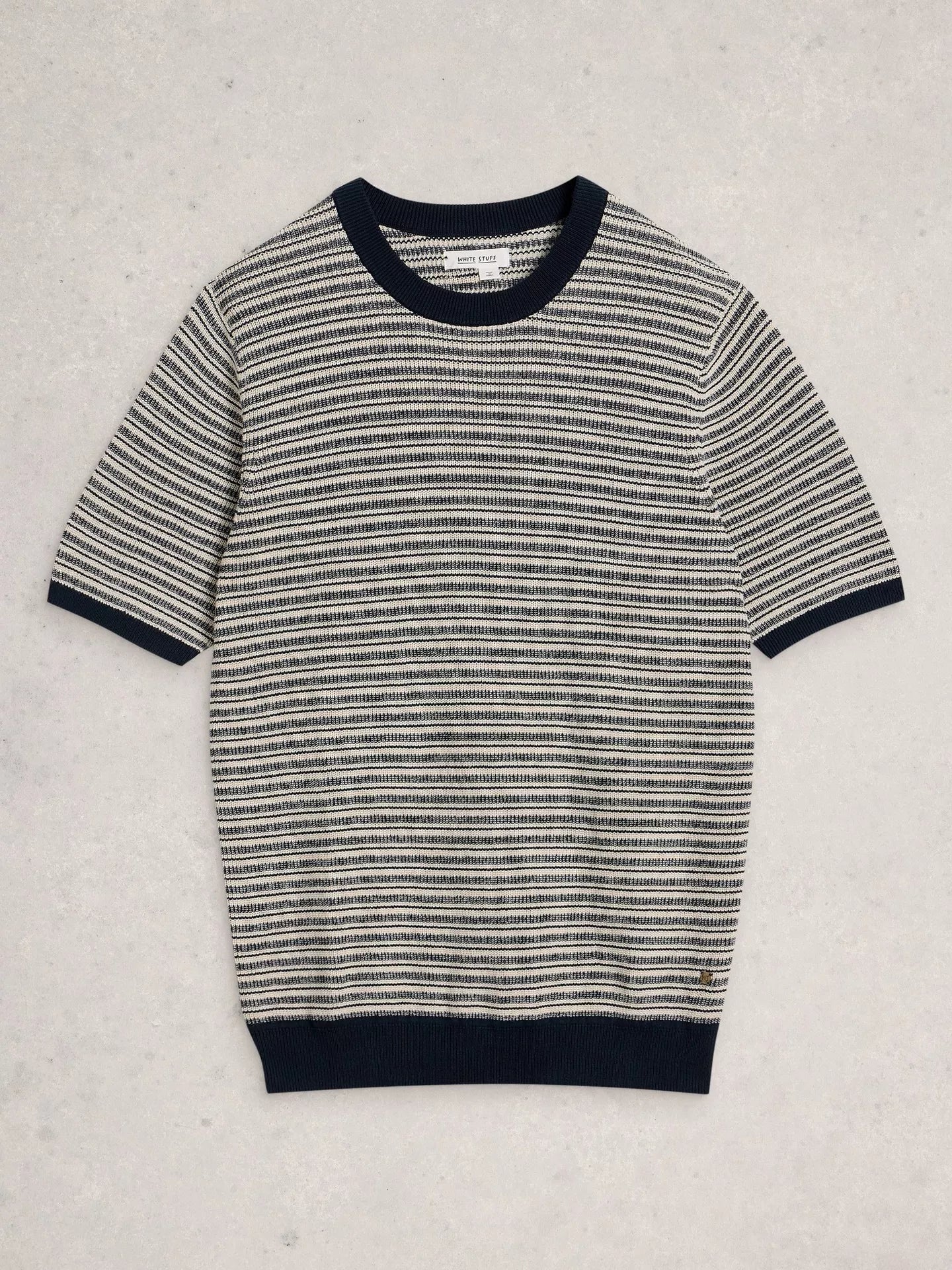 A short-sleeve knit sweater with horizontal black and off-white stripes, featuring solid black ribbed trim at the crew neck, sleeve cuffs, and hem, laid flat on a light textured background.