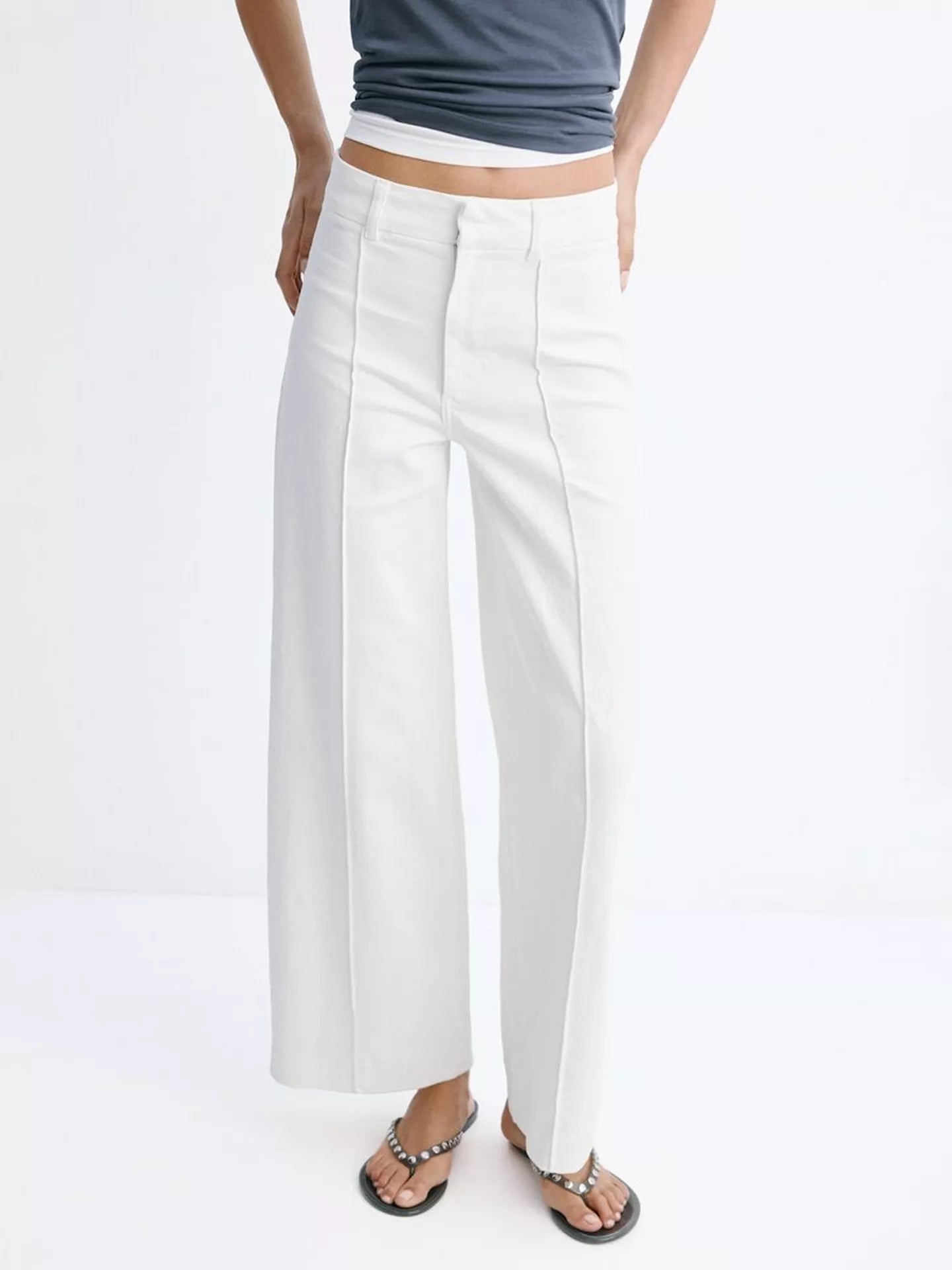 A person wearing white wide-leg cropped pants with a white top and black sandals, shown from the waist down against a plain white studio background.