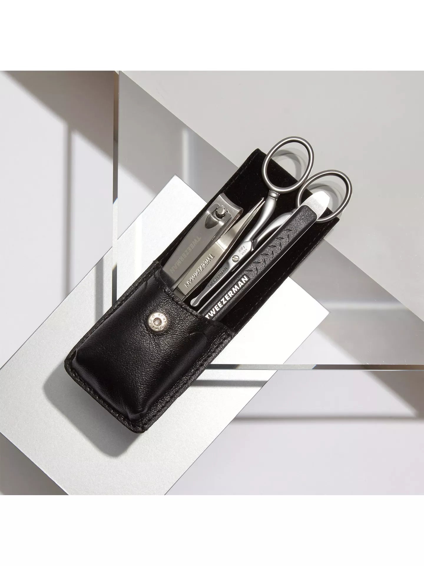 Manicure set with scissors, clippers, and mirror in a black leather case on a white background