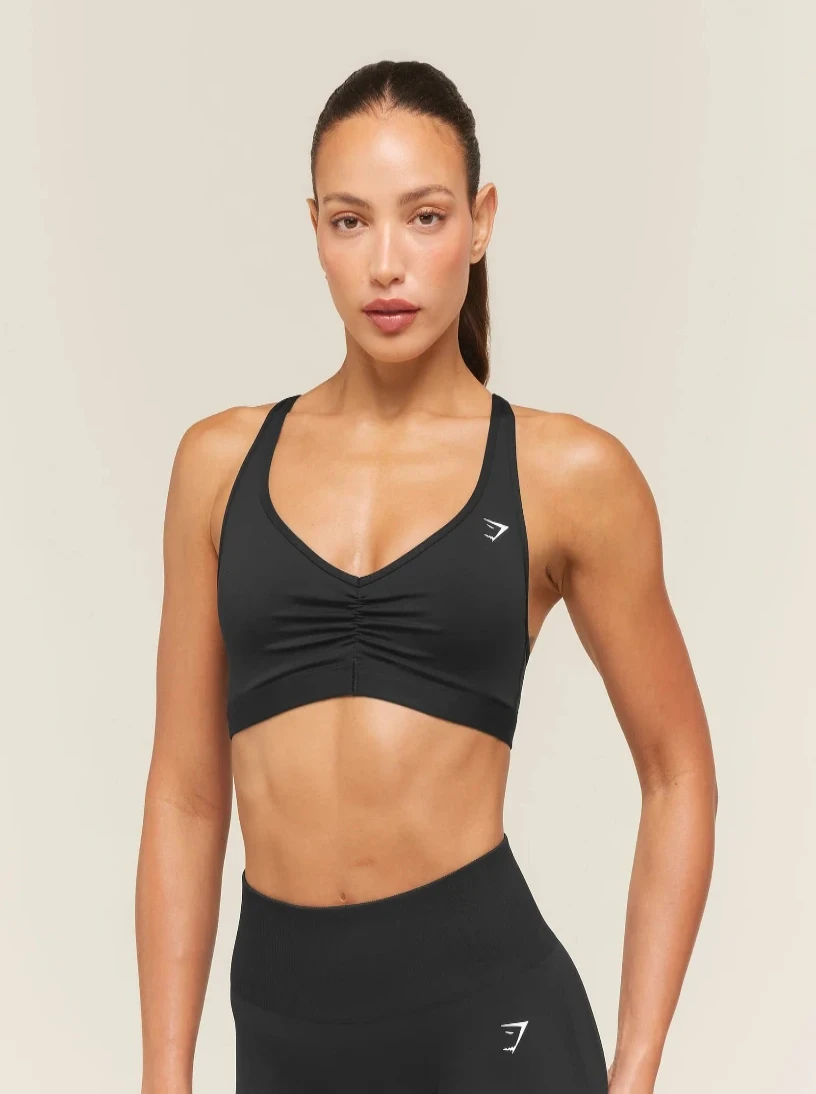 Woman wearing a black sports bra with a visible brand logo on a beige background
