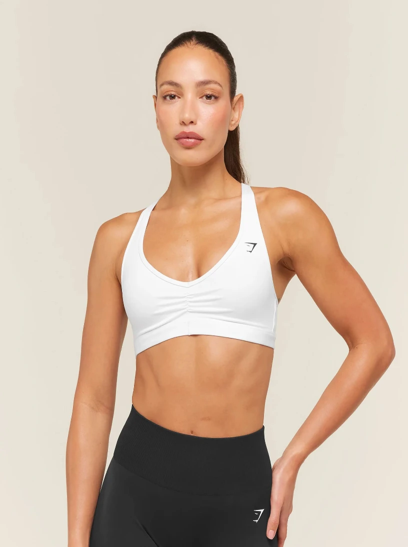 Woman wearing a white sports bra and black leggings on a beige background